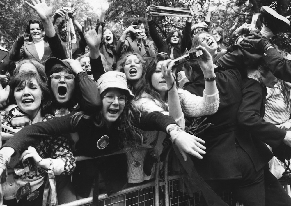 27th May 1975:  A crowd of excited fans of the American pop group The Osmonds wait behind a barrier in Eaton Square where the group is staying during a visit to London, hoping for a glimpse of the family.  (Photo by Central Press/Getty Images)